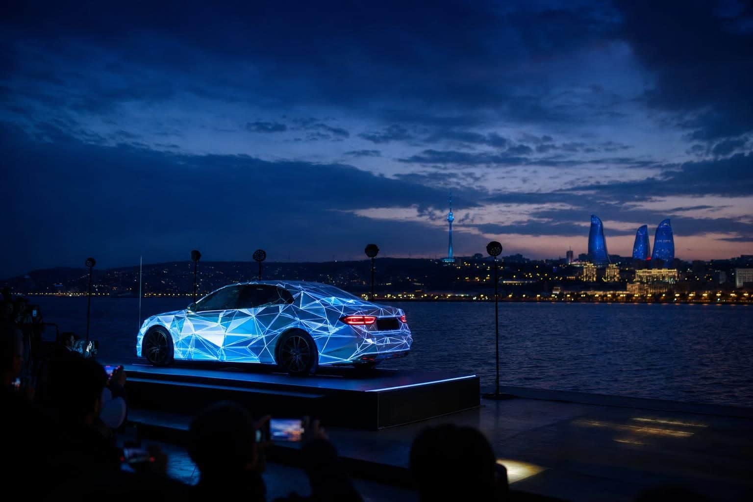 Unmarked sleek luxury sedan on stage platform, projection mapping wrapping the body in blue-white geometric patterns, National Flag Square, Baku