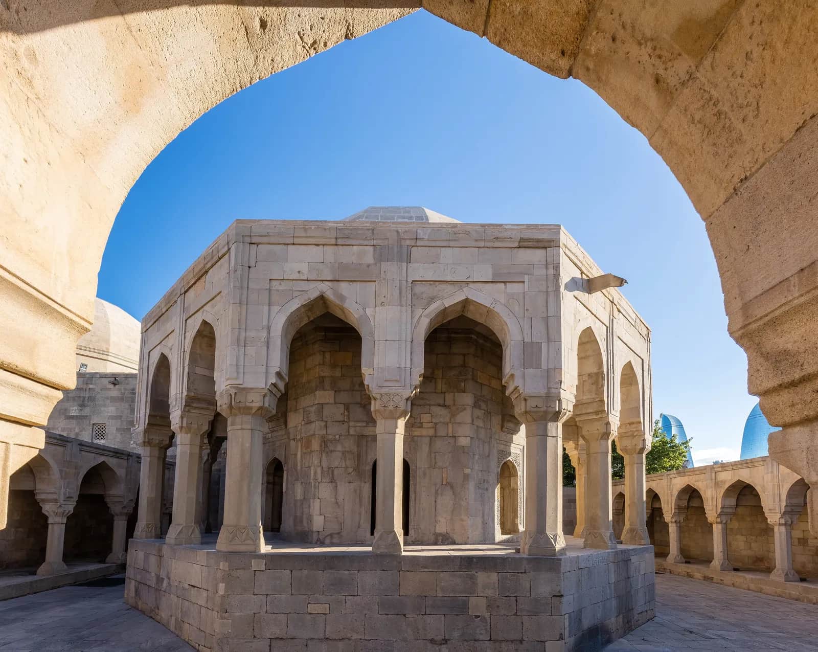 The octagonal divankhana rotunda of the Palace of the Shirvanshahs seen through an arch of the courtyard arcade, with the Flame Towers beyond