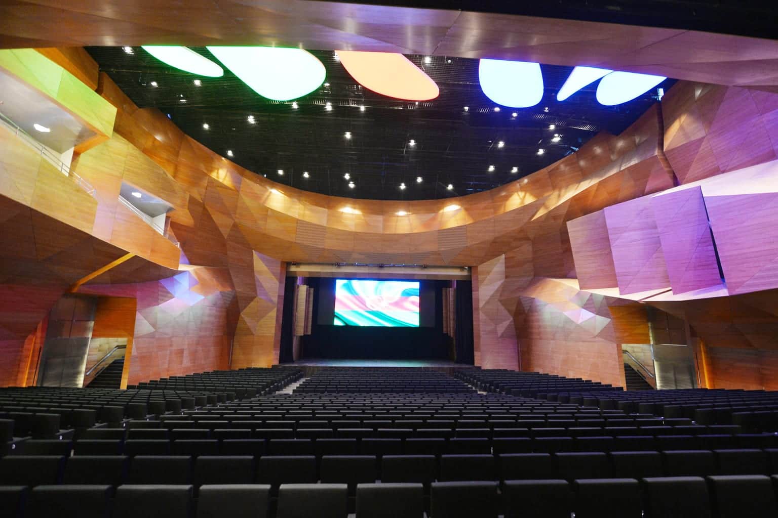 The tiered auditorium of Baku Congress Center, its timber walls lit in colour with a screen on the stage
