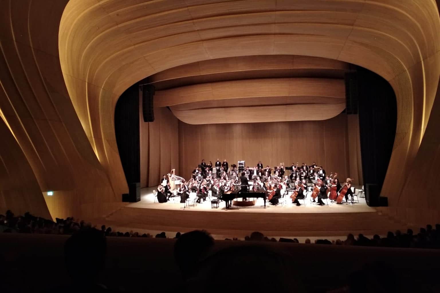 Orchestra on the stage of the Heydar Aliyev Center auditorium under the timber-clad curved ceiling
