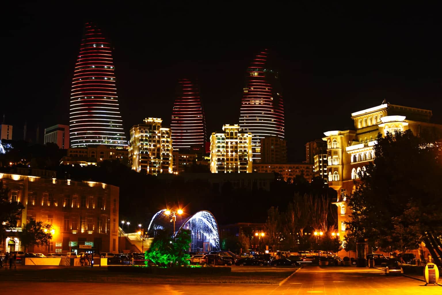 Baku at night with the Flame Towers lit red above the old city, seen from the boulevard side