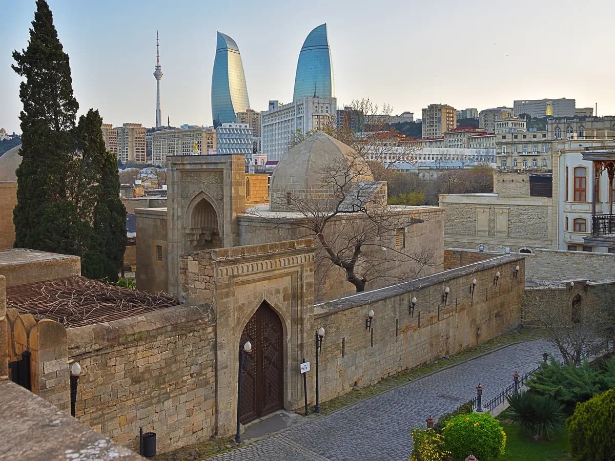 Domes and a carved portal of the Palace of the Shirvanshahs above the roofs of Baku's Old City, with the Flame Towers behind