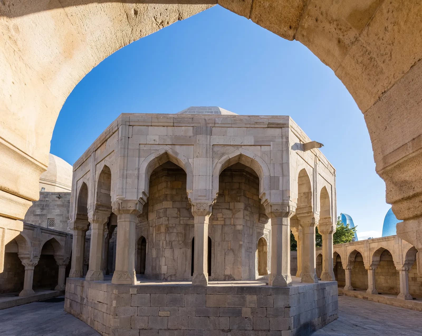 The octagonal divankhana rotunda of the Palace of the Shirvanshahs seen through an arch of the courtyard arcade, with the Flame Towers beyond