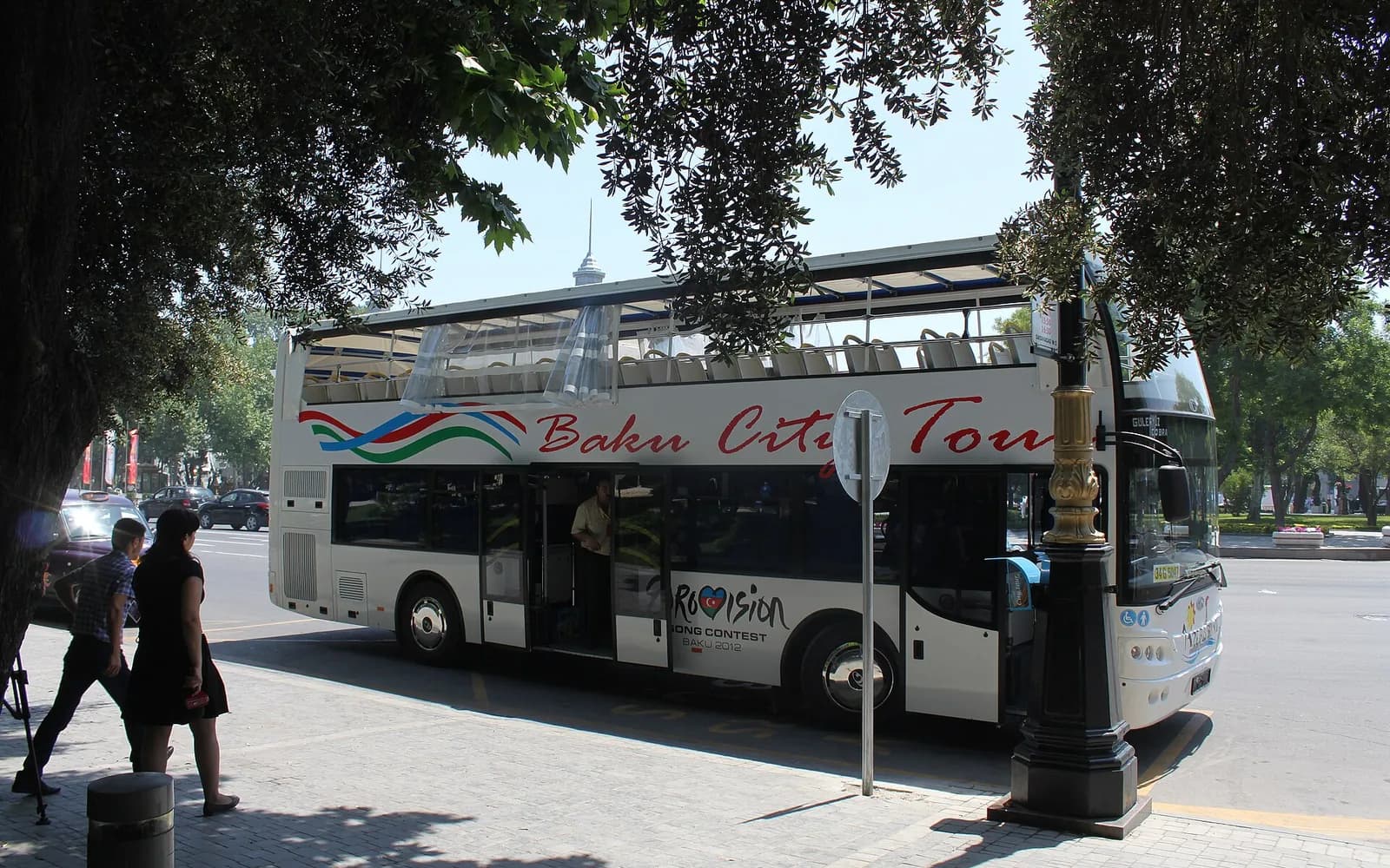 Open-top Baku City Tour bus stopped on a tree-lined central Baku street