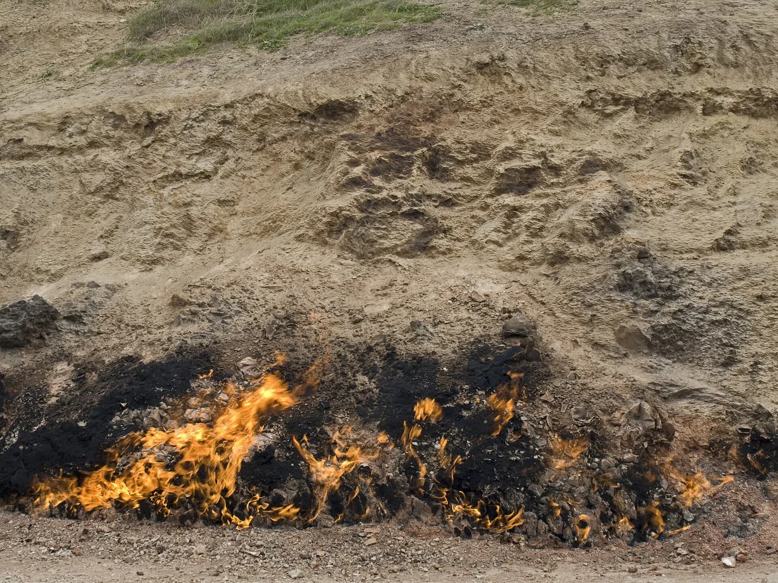 Natural flames burning along a rocky slope at Yanar Dag