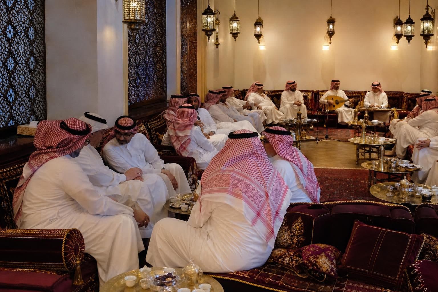 Around 25 men in traditional white kandura with red-and-white ghutra headdresses, in animated conversation, mostly, Baku