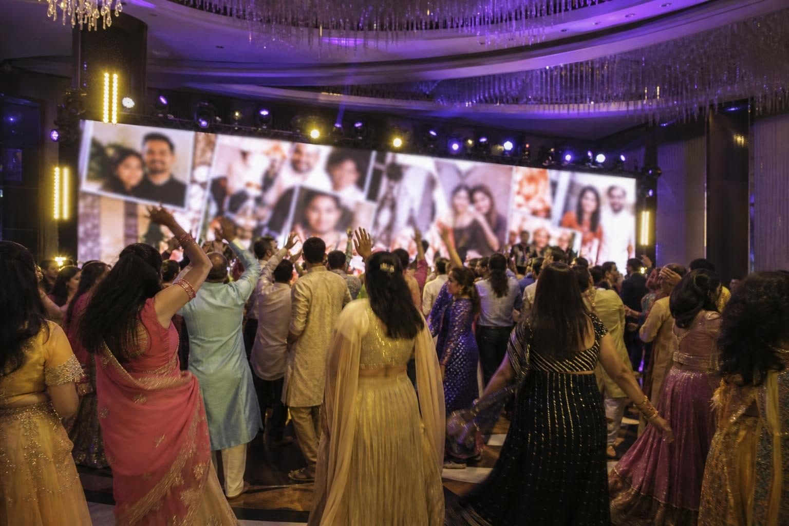 Around 40 guests in colorful Indian wedding attire dancing energetically, mostly /sides, arms raised, slight motion blur, Flame Towers, Baku