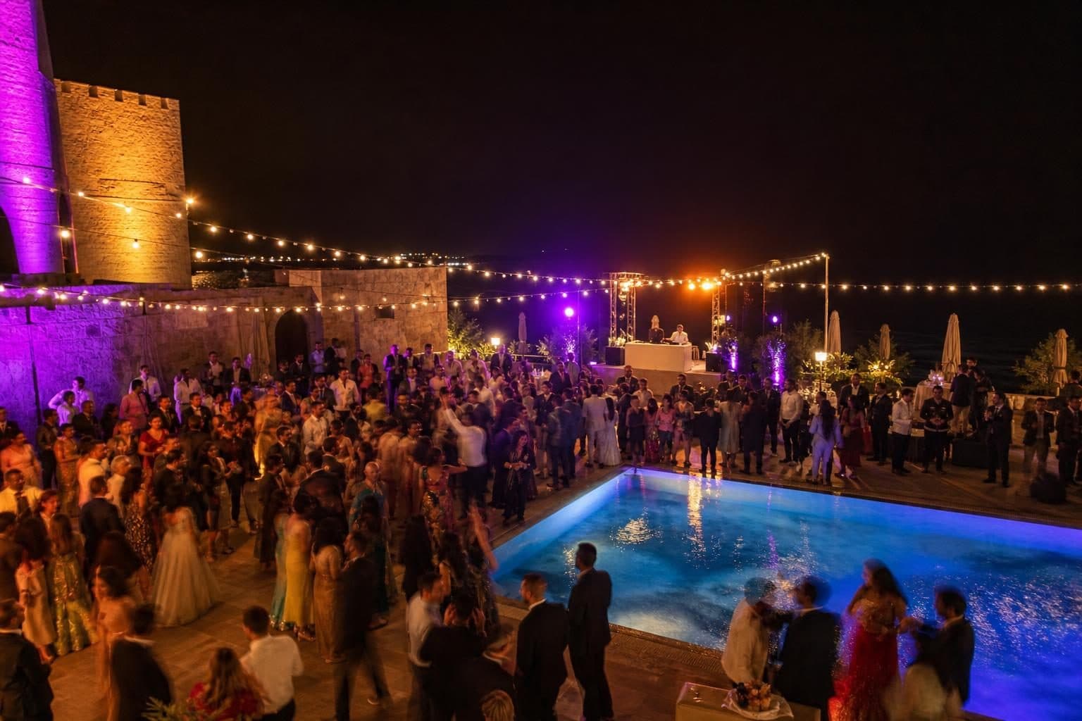 Packed dance floor over part of pool deck, around 50 guests dancing with motion blur, mix of formal Indian and Western evening attire, Bilgah, Baku