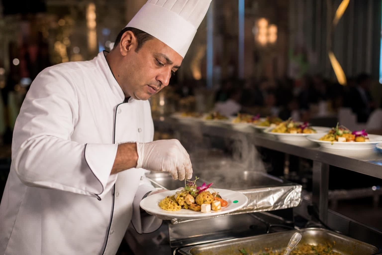 Male chef, gloved hands placing final garnish on plated jain-vegetarian dish, Baku