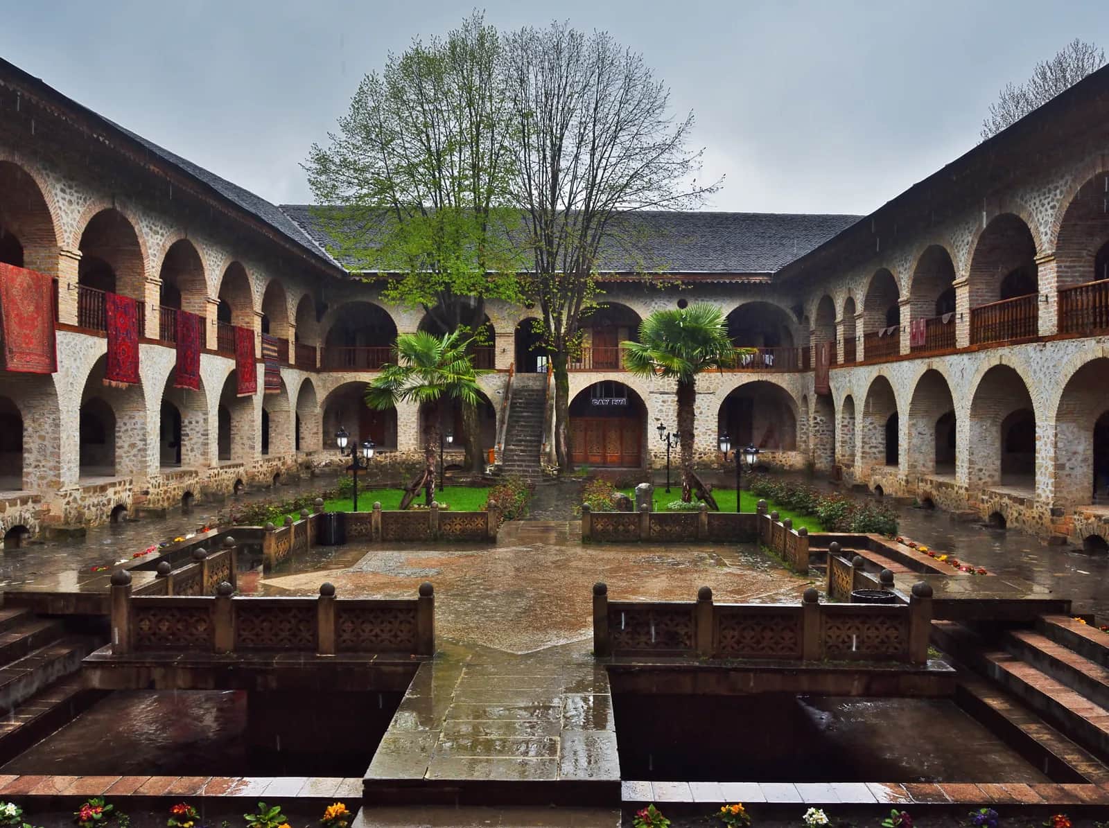 The arcaded inner courtyard of the Sheki Caravanserai after rain, carpets hung from the upper gallery