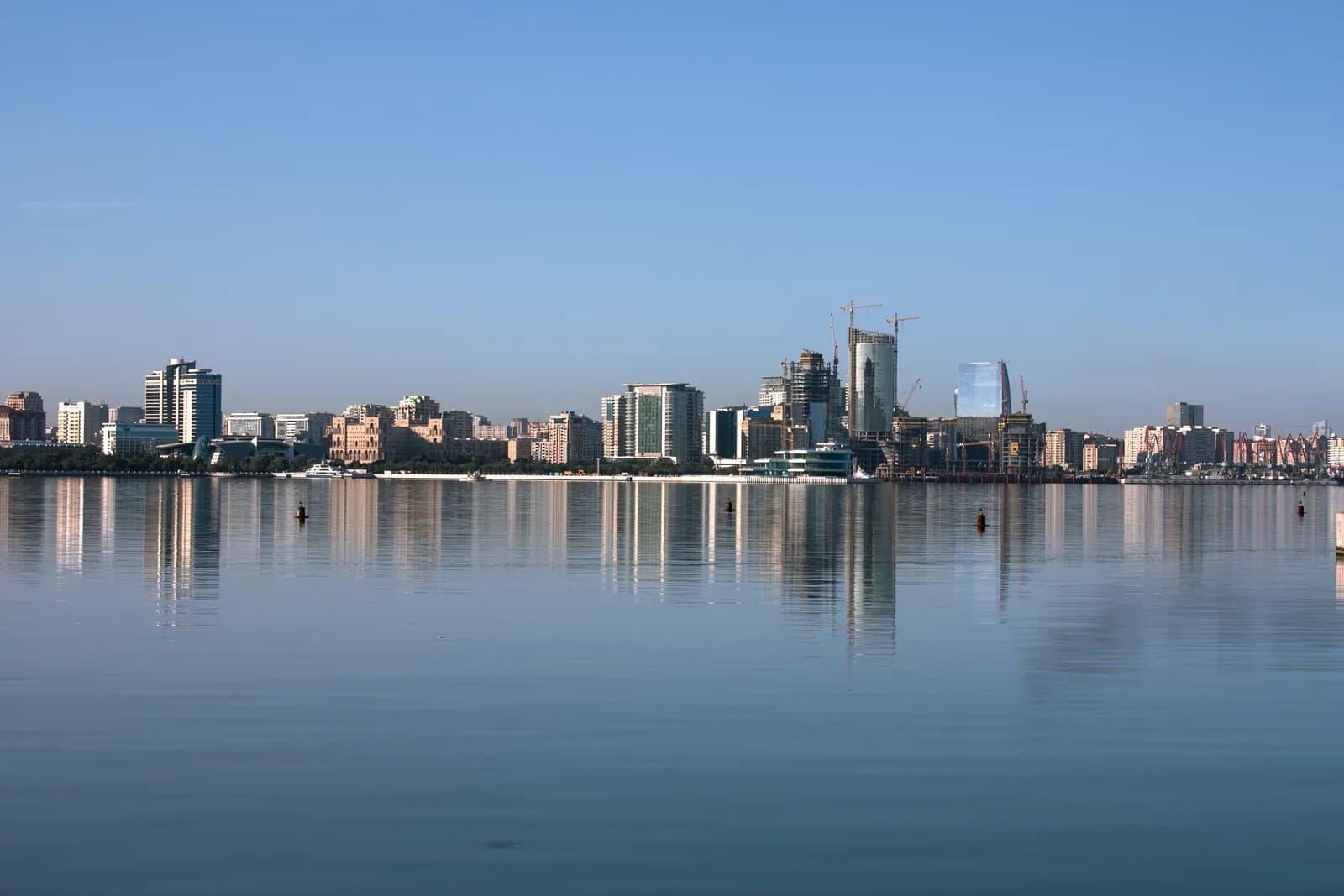 The Baku waterfront seen across the bay, with office blocks and tower cranes reflected in calm water