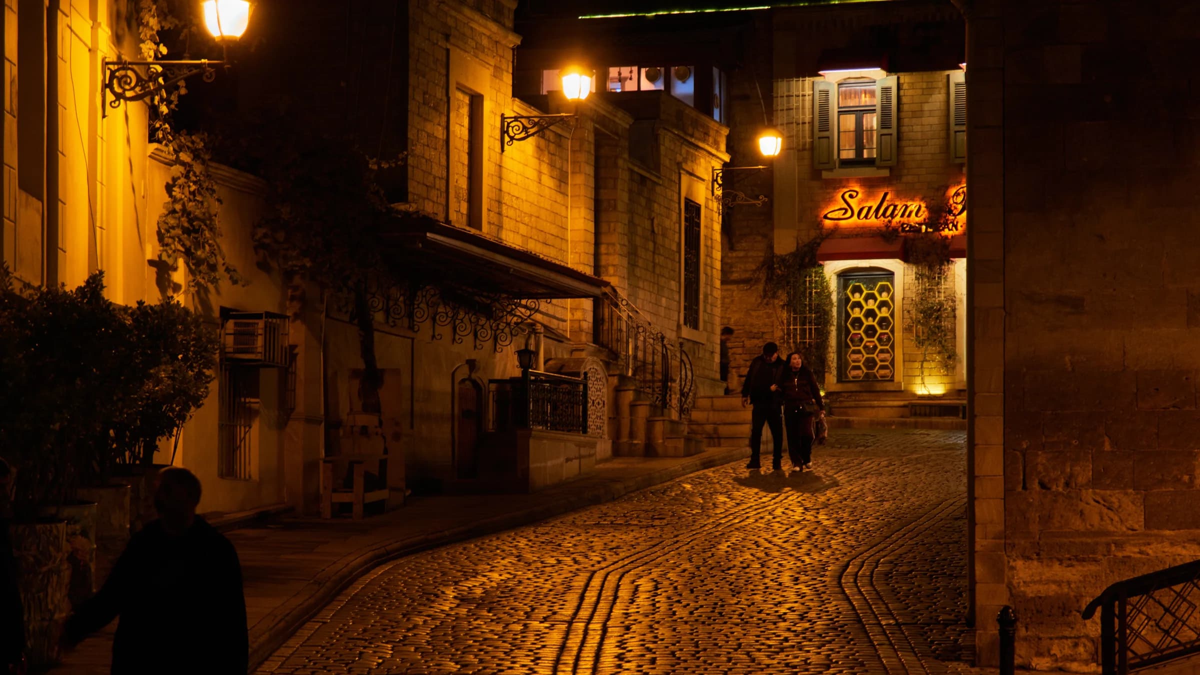 Pedestrians walking along a lantern-lit cobblestone street in Baku Old City