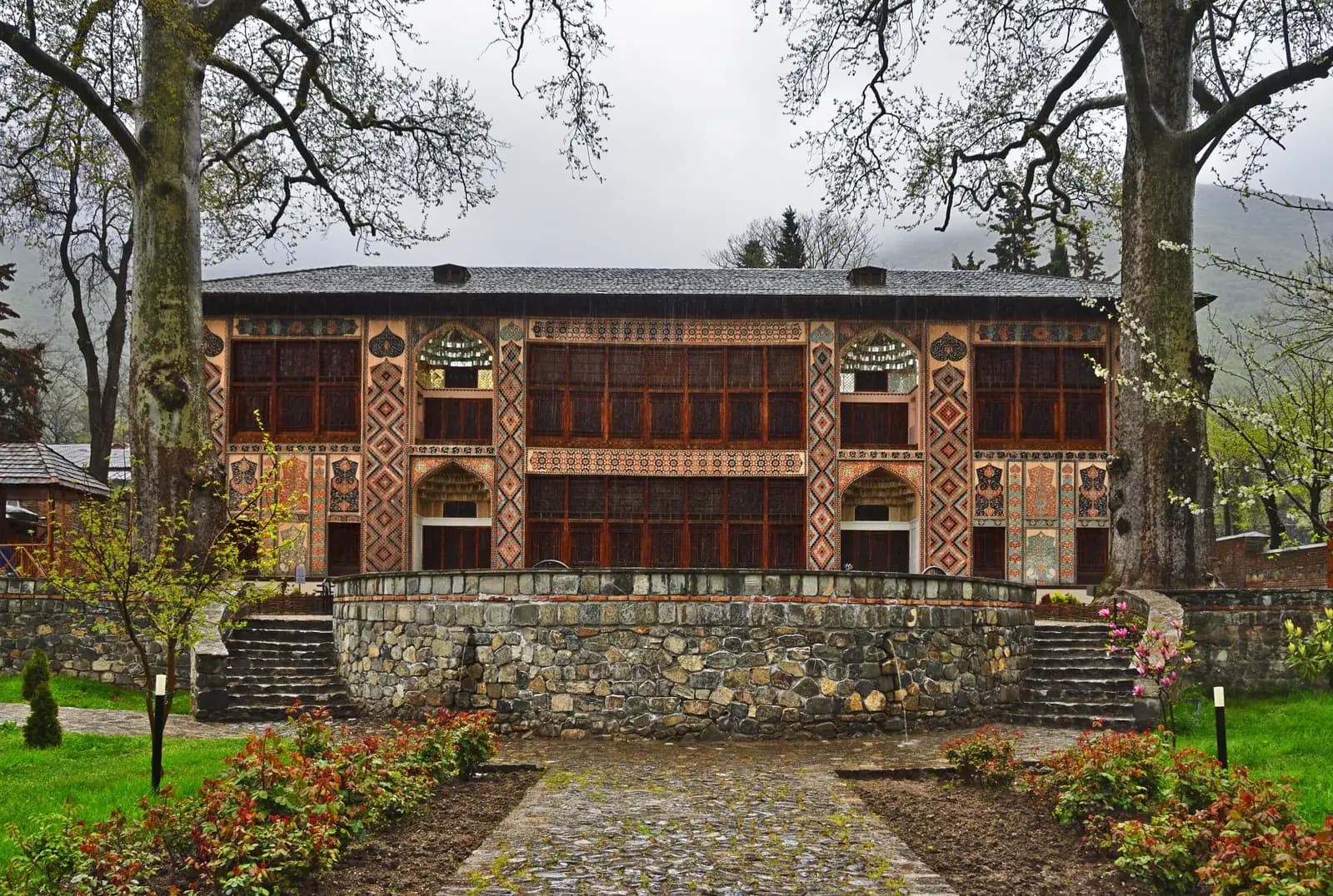 The painted facade of the Sheki Khan's Palace after rain, framed by old plane trees